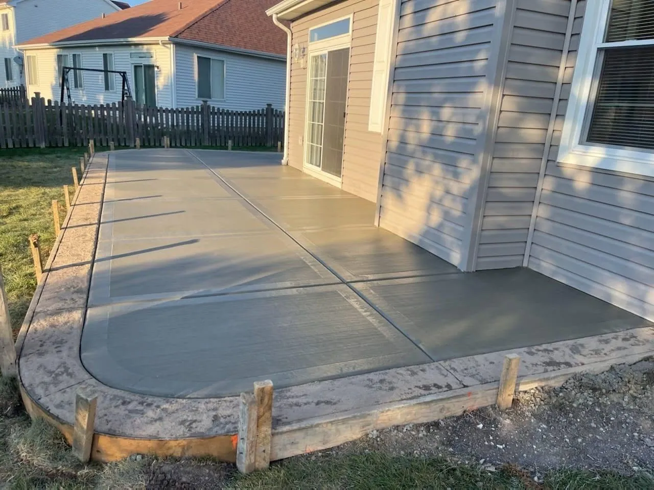 Curved broom-finish concrete patio wrapping a home at dusk by Ortiz Concrete Services
