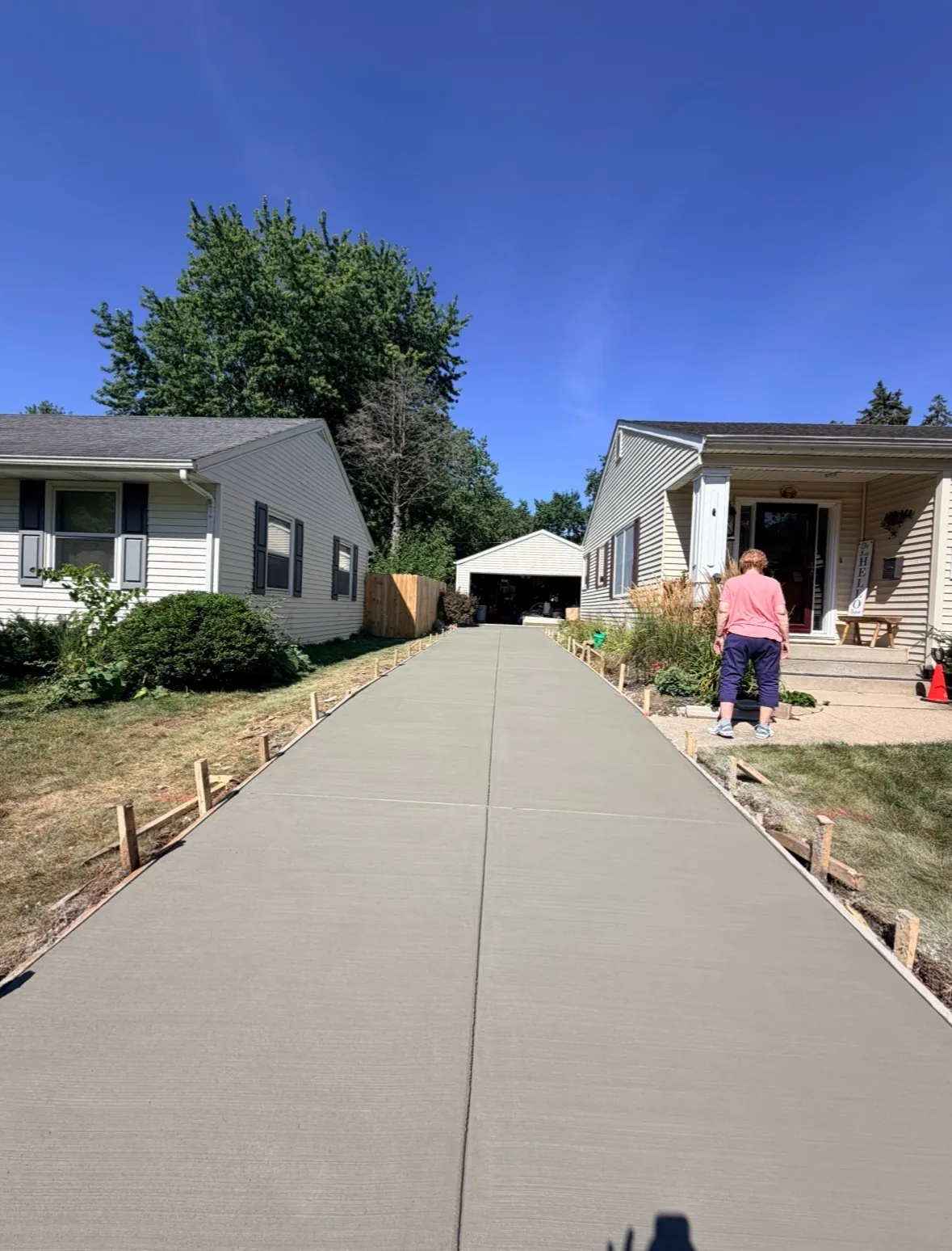 Freshly finished broom-finish concrete driveway running between two homes back to a detached garage, wood forms still staked along both edges