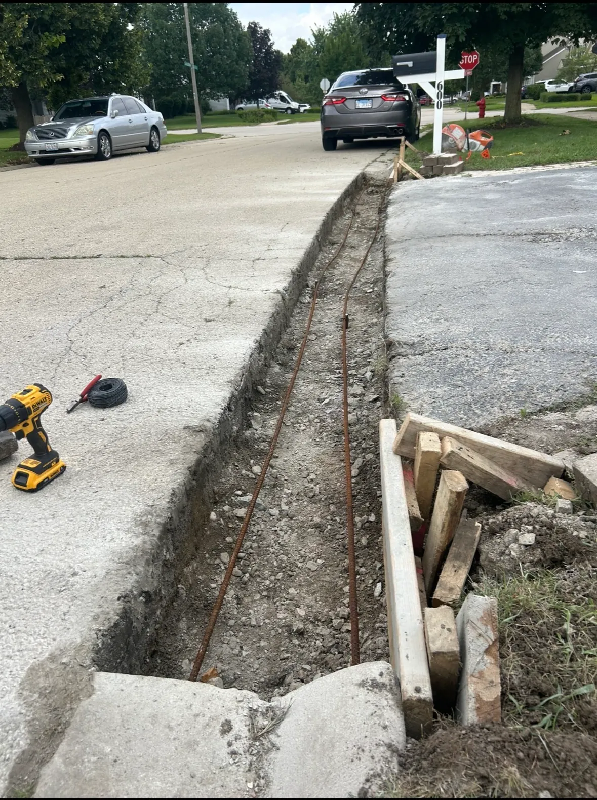Trench excavated along the edge of an existing concrete apron with steel rebar laid in place before a new pour, tie wire and a cordless drill set on the slab